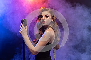 Side view portrait of beautiful female singer with microphone isolated over gradient blue purple background in neon