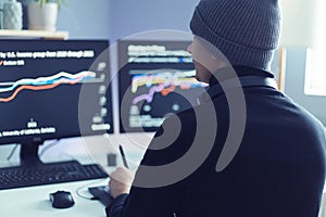 Side view portrait of business man wearing gray cap analyzing cryptocurrency market data, looking at computer monitors, waiting