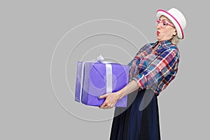Side view portrait of cheerful wondering modern grandma in white hat and checkered shirt standing and trying to hold giant big