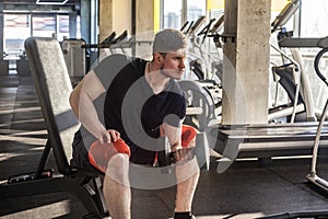 Side view portrait of concentration young adult man handsome athlete working out in gym, sitting on a bench and holding one