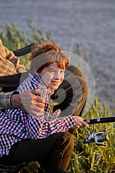 Side view portrait of cropped man and little grandson sitting near river and fishing