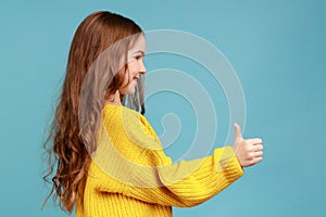 Side view portrait of cute charming little girl standing with thumb up, showing approved gesture.