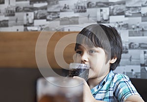 Side view portrait of Cute kid sitting on table drinking cold drink in restaurant, Little boy drinking soda or soft drink with str