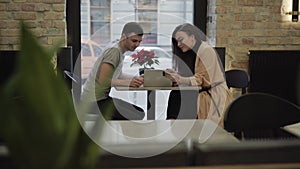 Side view portrait of happy millennial Caucasian couple surfing Internet on tablet and talking in cafe. Positive