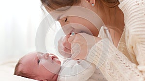Side view portrait of happy smiling mother stroking and cuddling her newborn baby lying on bed. Concept of family