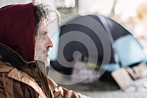 A side view portrait of homeless beggar man sitting outdoors. Copy space.