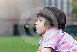 Side view portrait of little boy looking out with thinking face, Head shot Kid lying down on grass in the park, Child relaxing out
