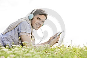 Side view portrait of man listening to music on MP3 player using headphones in park against clear sky