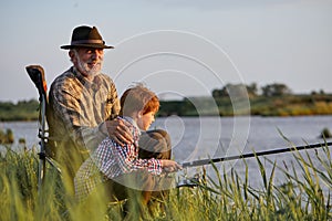 Side view portrait of man and little grandson sitting near river and fishing