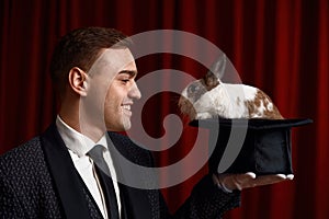 Side view portrait of man magician looking on rabbit appeared in hat photo