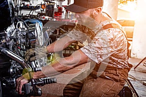 Side view portrait of man working in garage repairing motorcycle and customizing it photo
