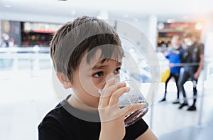 Side view Portrait of mixed race young kid sitting on table drinking cold drink in restaurant, Toodler drinking soda or soft drink