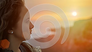 Side view portrait of a pensive young woman at sunset with a coastal city and mountains in the background. The concept of travel