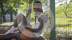 Side view portrait of positive African American basketball player taking selfie on smartphone. Young man sitting on