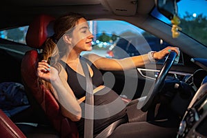 Side view portrait of pregnant woman driving car at night.