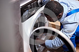 Side view portrait of professional afro technician examining broken washing machine