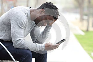 Sad black man complaining checking mobile phone