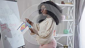 Side view portrait of serious concentrated smart African American woman in eyeglasses analyzing diagrams standing at