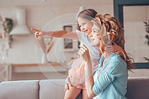 Side view portrait of small girl pointing with finger and showing something to her mother sitting on the sofa