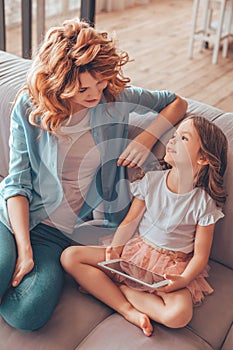 Side view portrait of small girl pointing with finger and showing something to her mother sitting on the sofa