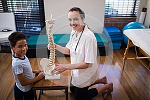 Side view portrait of smiling female therapist and boy kneeling with artificial spine