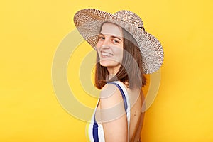 Side view portrait of smiling woman wearing striped swimming suit and sun hat isolated on yellow background looking at camera with