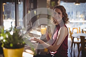 Side view portrait of smiling young woman holding fresh juice glass at coffee shop