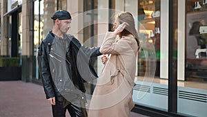 Side view portrait of stylish gay man criticizing young Caucasian woman outfit standing on city street. Confident