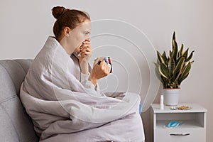 Side view portrait of unhealthy woman sitting on cough and coughing, drinking tea, suffering influenza, having high temperature