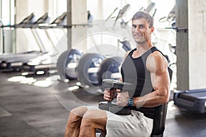 Side view portrait of young adult man muscular built handsome athlete working out in a gym, sitting on a weightlifting machine and