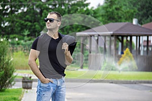 Side view portrait of a young fashion man wearing sunglasses and holding jacket on his shoulder on the street