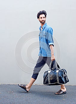 Side view portrait of a young man walking with travel bag