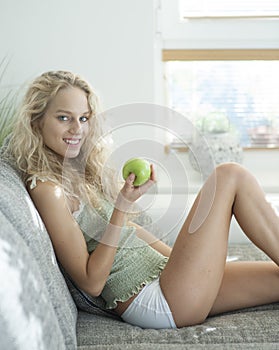 Side view portrait of young woman holding apple while sitting on sofa in house