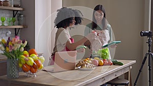 Side view of positive cheerful African American young woman holding ingredients for healthful organic vegan salad as