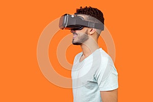 Side view of positive gamer, brunette man watching video or playing virtual reality game. isolated on orange background