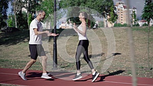 Side view of positive sportsman and sportswoman jogging on urban running track. Wide shot of smiling man and woman