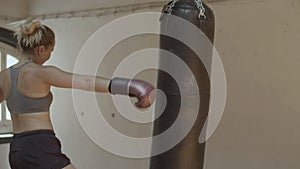 Side view of powerful woman punching and kicking heavy bag