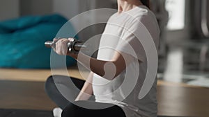 Side view pregnant unrecognizable woman lifting dumbbell sitting on exercise mat at home in the morning. Caucasian young