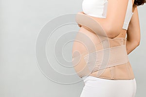 Side view of pregnant woman in underwear wearing pregnancy bandage at gray background with copy space. Close up of orthopedic