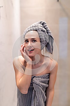 Side view of pretty female with towel on head and in bathrobe posing. Portrait of woman with naked shoulder enjoying time after