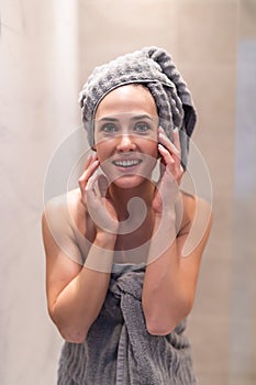 Side view of pretty female with towel on head and in bathrobe posing. Portrait of woman with naked shoulder enjoying time after