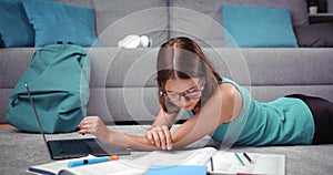 Side view of pretty girl lying on floor and typing on laptop