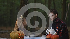 Side view pretty girl touching nose of vampire sitting in forest on Halloween scaring creature making faces. Caucasian