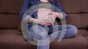 A side view of a pretty pregnant woman is sitting on the sofa and stroking her belly. Pregnant woman relaxing at home on the couch