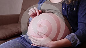 A side view of a pretty pregnant woman is sitting on the sofa and stroking her belly. Pregnant woman relaxing at home on the couch