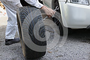 Side view of professional automotive mechanic man in uniform holding tire for fixing car at the garage background. Auto repair ser