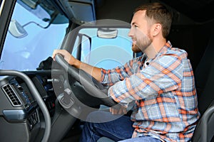 Side view of professional driver behind the wheel in truck's cabin.