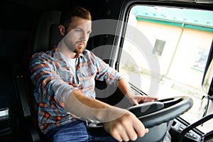 Side view of professional driver behind the wheel in truck's cabin.