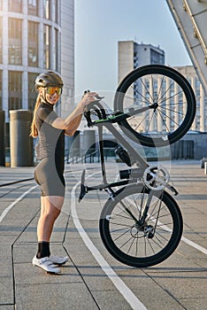 Side view of professional female cyclist in black cycling garment and protective gear smiling at camera, posing with her