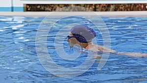 Side view of a professional female swimmer with goggles at the pool. A woman swimmer dives into a pool of water. Close